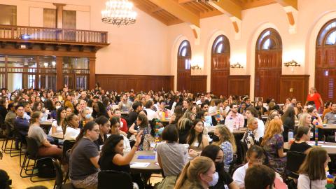 Teams of people sitting at round tables in a large ballroom. 