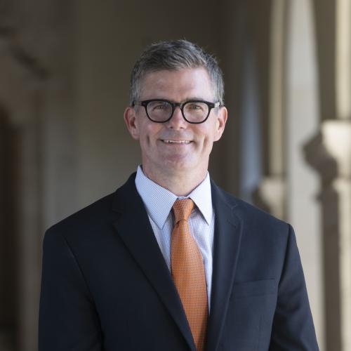 Man with glasses in suit and burnt orange tie smiling