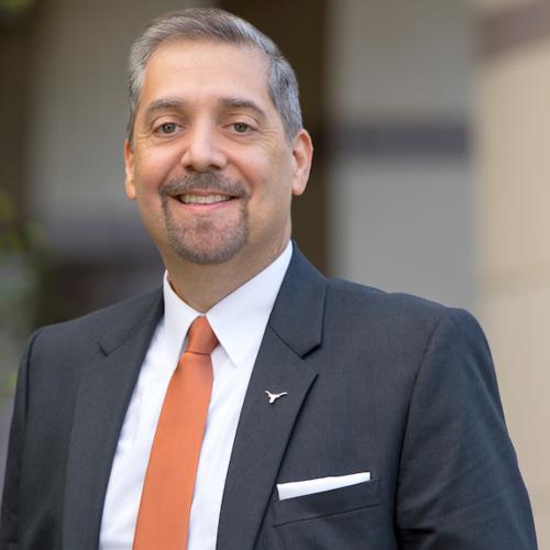 Man with glasses in suit and burnt orange tie smiling