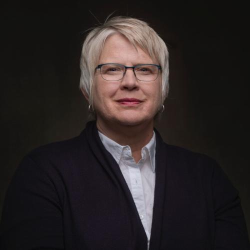 Sarah Sloan Person with close-mouth smile and glasses, a black jacket, and a white shirt.