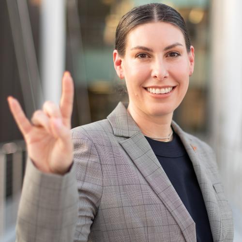 A woman with brown hair that's pulled back smiling and showing the Hook 'Em Horns sign. 