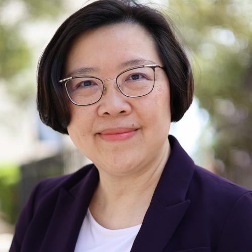 Picture of a woman with glasses who is smiling and wearing a blazer and shirt. 