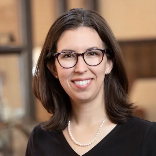 Woman with glasses, brown hair, and a black shirt smiling 