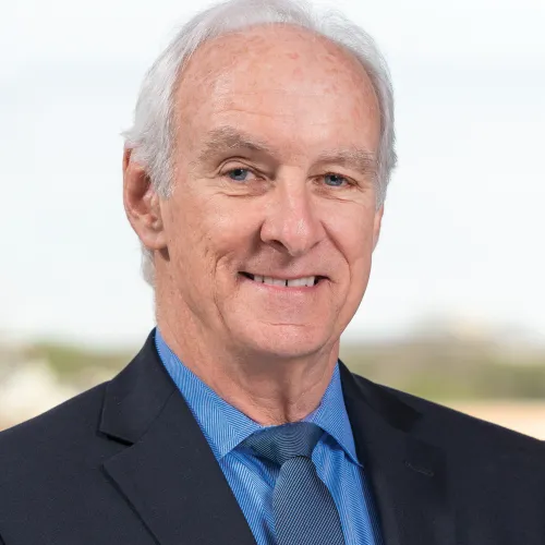 Man in a suit, blue shirt, and blue tie smiling 