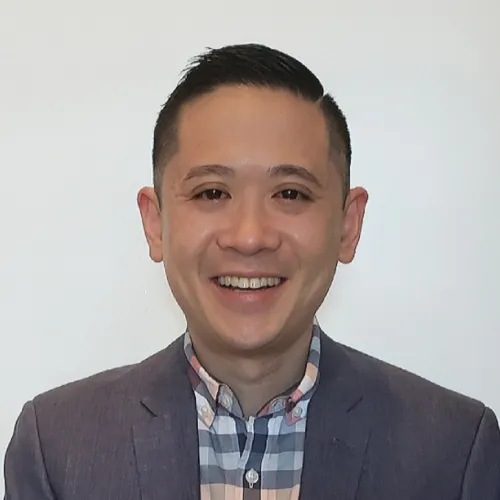 Man with short black hair in gray blazer smiling.