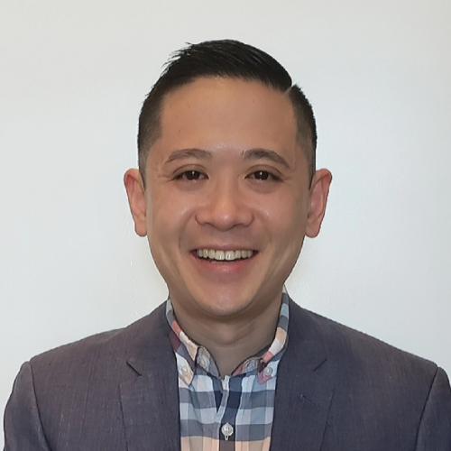 Man with short black hair in gray blazer smiling.