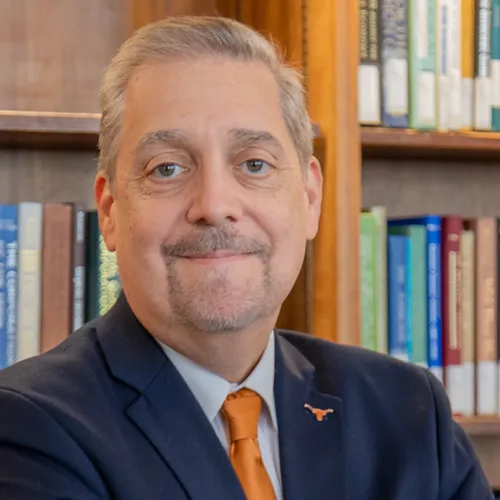 Man smiling at the camera. He is wearing a navy suit and orange tie. 