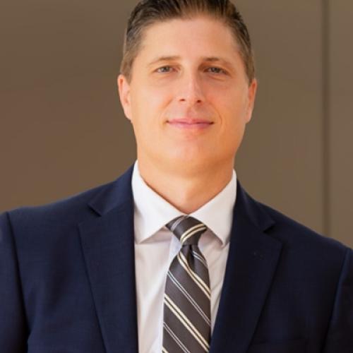 Man smiling at camera wearing a suit and tie and a white shirt. 