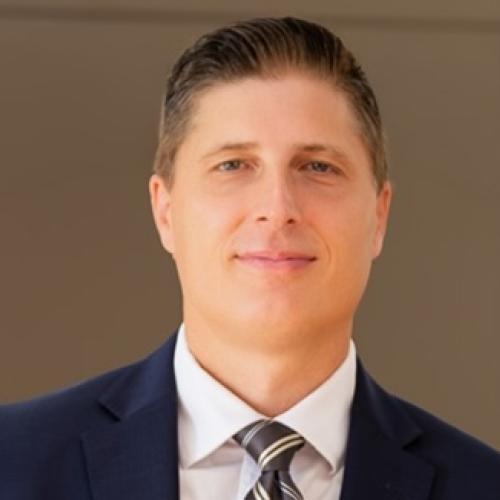 Man smiling at camera wearing a suit and tie and a white shirt. 